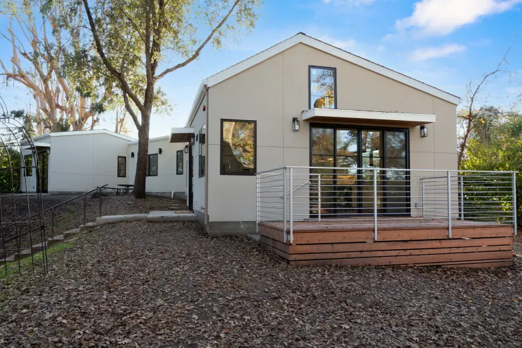 Finished ADU with a gabled roof, black-framed windows, and a cable-rail deck, set among mature oaks
