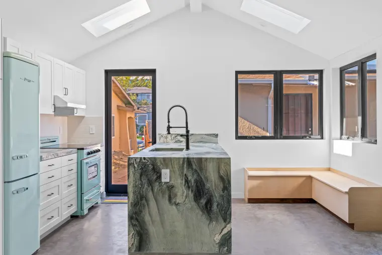Vaulted kitchen with skylights, a waterfall-edge stone island, mint retro refrigerator and range, and a built-in bench under black-framed windows